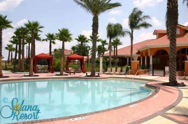 A swimming pool with a red canopy, palm trees, and a building with a red roof.
