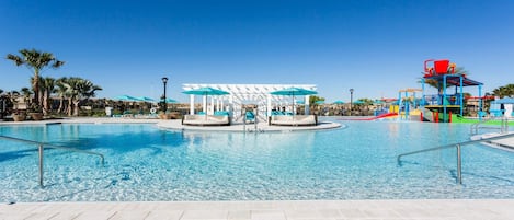 A large outdoor swimming pool with lounge chairs and umbrellas, a water play area, and a covered seating area.