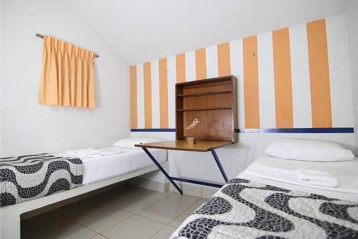 Habitación de hotel con dos camas, una mesita de madera, un estante en la pared y un diseño de pared a rayas.