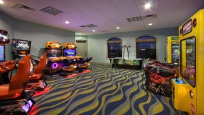 Una sala de juegos con varios juegos de carreras y de arcade, una mesa de billar y ventanas amplias.