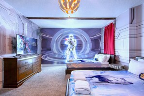 Un dormitorio con temática de Star Wars, que incluye una cama con edredón de Star Wars, un aparador y un televisor mostrando una película de Star Wars.