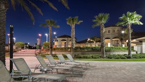 A nighttime outdoor seating area with lounge chairs and palm trees, leading to a building with multiple balconies and a stone wall. - Star Wars Suite & Epic Spider-Man Game Room (Kissimmee)