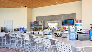 Una zona de bar con diversas opciones de asientos, una pantalla de televisión y una variedad de bebidas y botellas.