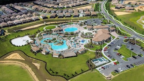 An aerial view of a resort with multiple swimming pools, a parking area, and a golf course.