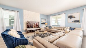A living room with a blue sofa, beige sofa, and a blue armchair. There is a TV on a wooden stand, a lamp, and a coffee table. - Star Wars Suite & Epic Spider-Man Game Room (Kissimmee)