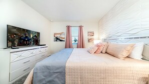 Un dormitorio con cama, televisor en una cómoda, ventana con cortinas y decoración en la pared.