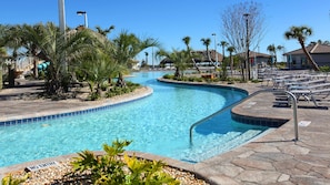 A swimming pool with a curved design, surrounded by palm trees and lounge chairs.