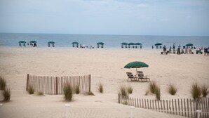 Una spiaggia con file di ombrelloni verdi e lettini, una recinzione di legno e l'oceano sullo sfondo.