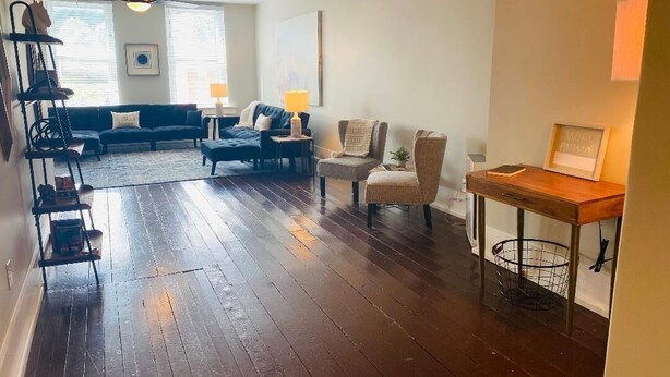 A spacious living room with a dark wooden floor, a sofa set, a coffee table, and a side table with a lamp. - Amazing 1 Bedroom Apartment, Downtown Jonesborough (Jonesborough)