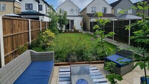 A backyard with a grassy lawn, a wooden fence, and outdoor furniture including a wicker sofa and a table. - Exclusive Palm House,  Nature, Amenities, Garden (Addlestone)