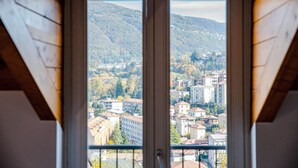 A view from a window with a wooden frame, overlooking a town with buildings and hills in the background. - MyHomeInComo - Modern Luxury Attic (Como)