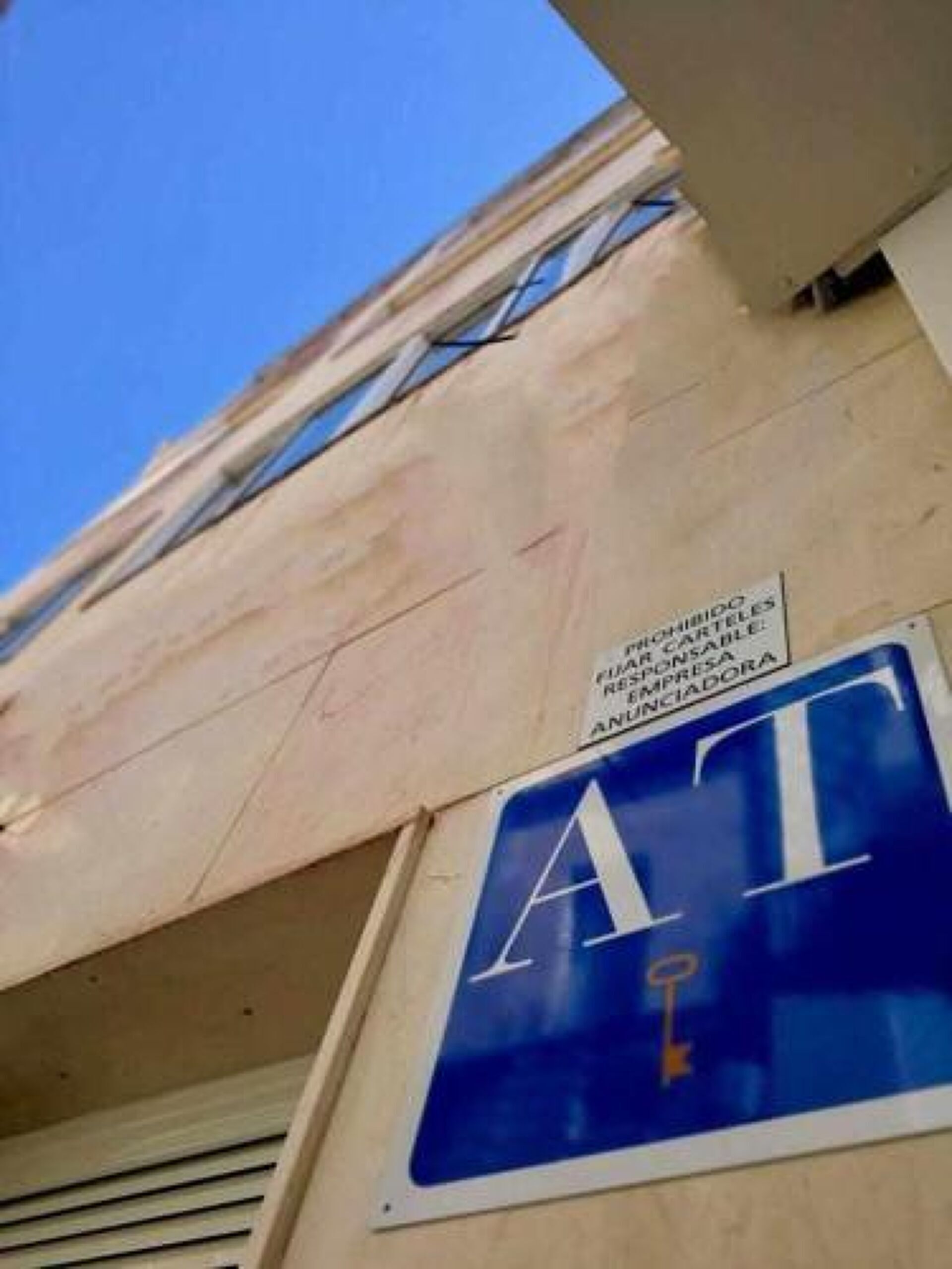 Un edificio con un letrero azul que muestra una 'A' blanca y un símbolo de llave, y un cartel superior que indica que es una 'FARMACIA RESPONSABLE ANCIADORA'.