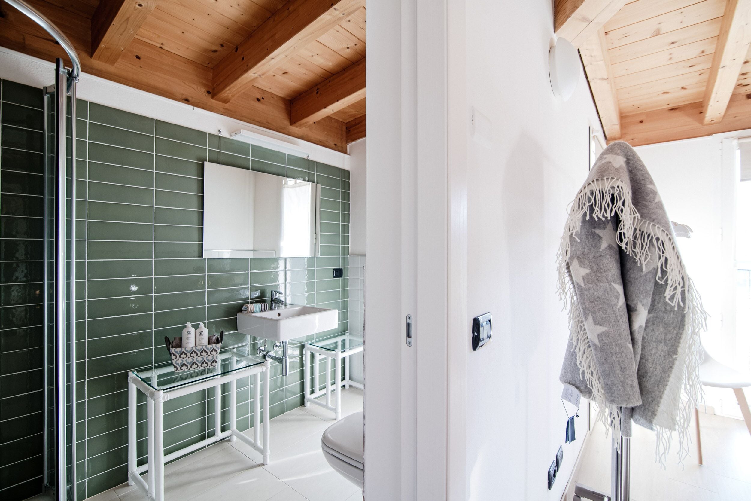 A bathroom with green tiles, a white sink, and a glass shower enclosure.