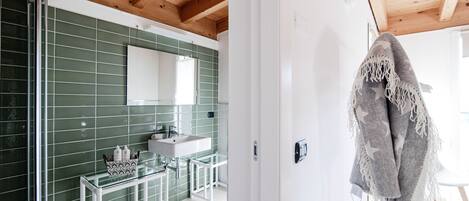 A bathroom with green tiles, a white sink, and a glass shower enclosure.