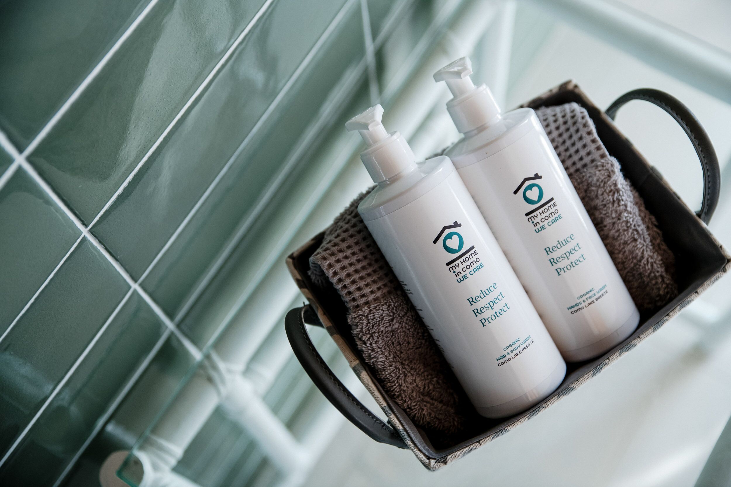 A bathroom with a tiled wall and a metal container holding two bottles of shampoo and conditioner.