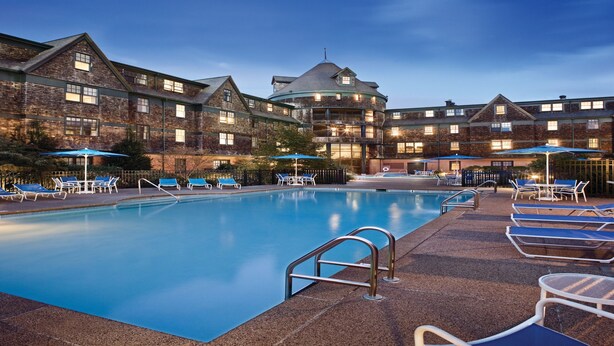 A swimming pool with lounge chairs and umbrellas, surrounded by a brick building with multiple windows and balconies.
