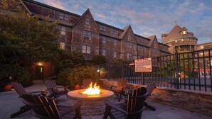 A patio with a fire pit and Adirondack chairs, a brick building with a circular tower, and a sign with fire rules.