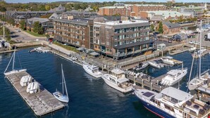 A marina with boats docked, a building with multiple floors, and a river in the background.