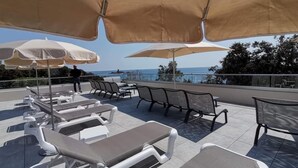 A rooftop terrace with lounge chairs and umbrellas, overlooking a scenic view.