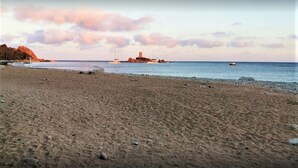 A beach with a rocky shoreline, a small island with a tower, and sailboats in the distance.