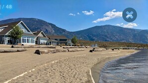 Une plage bordée d’une rangée de maisons, avec des montagnes en arrière-plan.