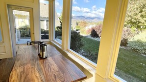 Un coin repas avec une table et des chaises en bois, de grandes fenêtres donnant sur un jardin et des montagnes.