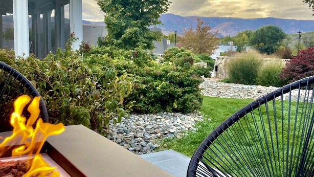 Une terrasse avec un barbecue, deux chaises et une vue sur une maison et des montagnes.
