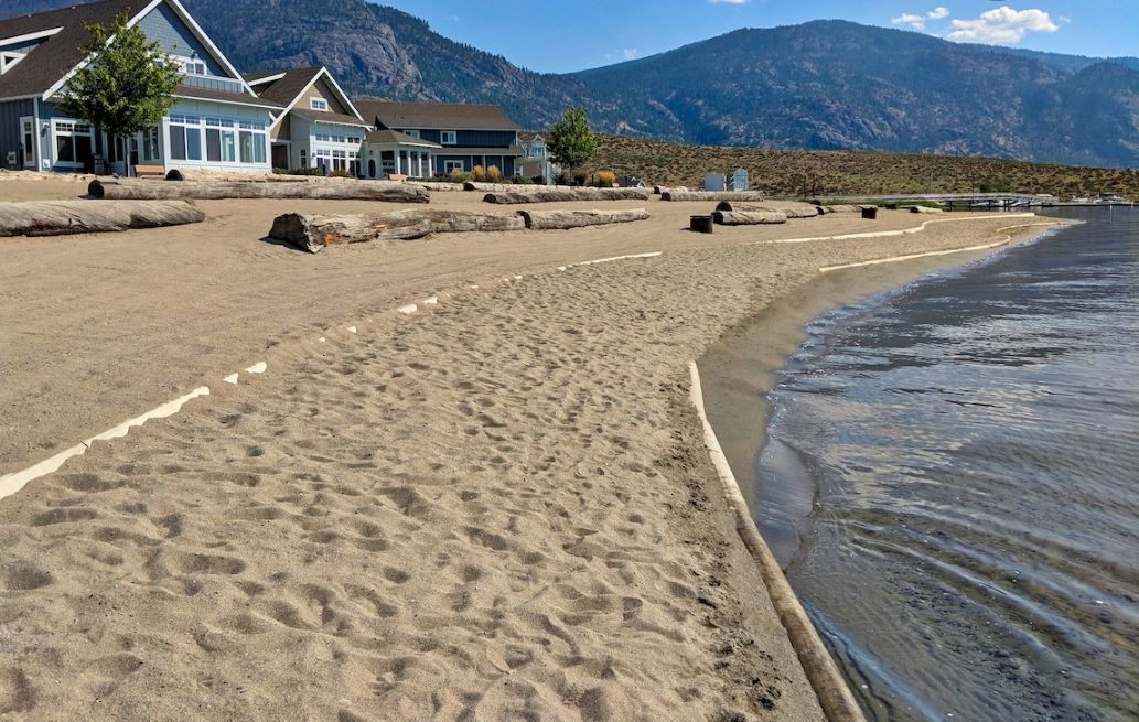 Une plage bordée d’une rangée de maisons, avec des montagnes en arrière-plan.