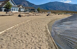 Une plage bordée d’une rangée de maisons, avec des montagnes en arrière-plan.