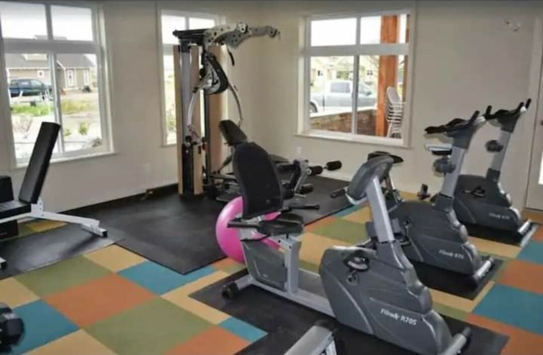 A gym with exercise equipment, including treadmills and a weight machine, and large windows.