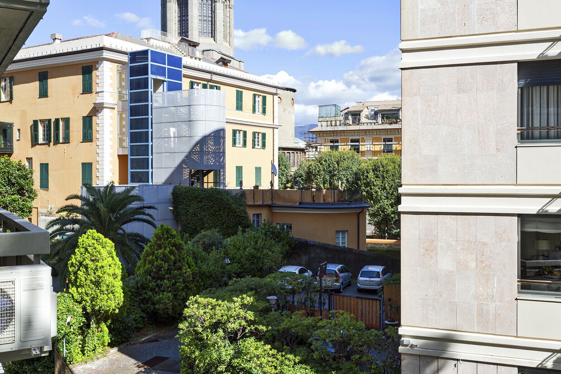 A courtyard with a modern building, a traditional building, and parked cars.