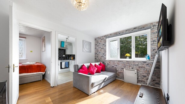 Een moderne woonkamer met een grijze bank, rode kussens, een houten salontafel en een aan de muur bevestigde televisie.