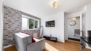 Een moderne woonkamer met een grijze bank, een bakstenen muur, een groot raam en een flatscreen televisie aan de wand.