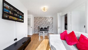 Een moderne woonkamer met een flatscreentelevisie, een eethoek met een bakstenen muur, en een heldere plafondlamp.