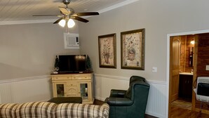 Un salon avec un canapé à carreaux, un fauteuil vert, un téléviseur posé sur un meuble et deux tableaux floraux encadrés accrochés au mur.