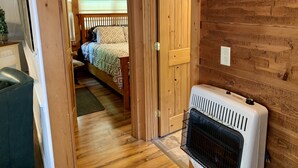 Un intérieur en bois avec un lit, un radiateur et une porte donnant sur une autre pièce.