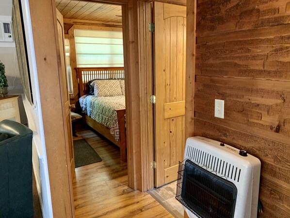 Un intérieur en bois avec un lit, un radiateur et une porte donnant sur une autre pièce.