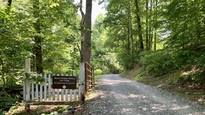 Un chemin de gravier mène à une porte en bois sur laquelle est apposée une plaque indiquant « Byron Herbert Reece Farm Village ».