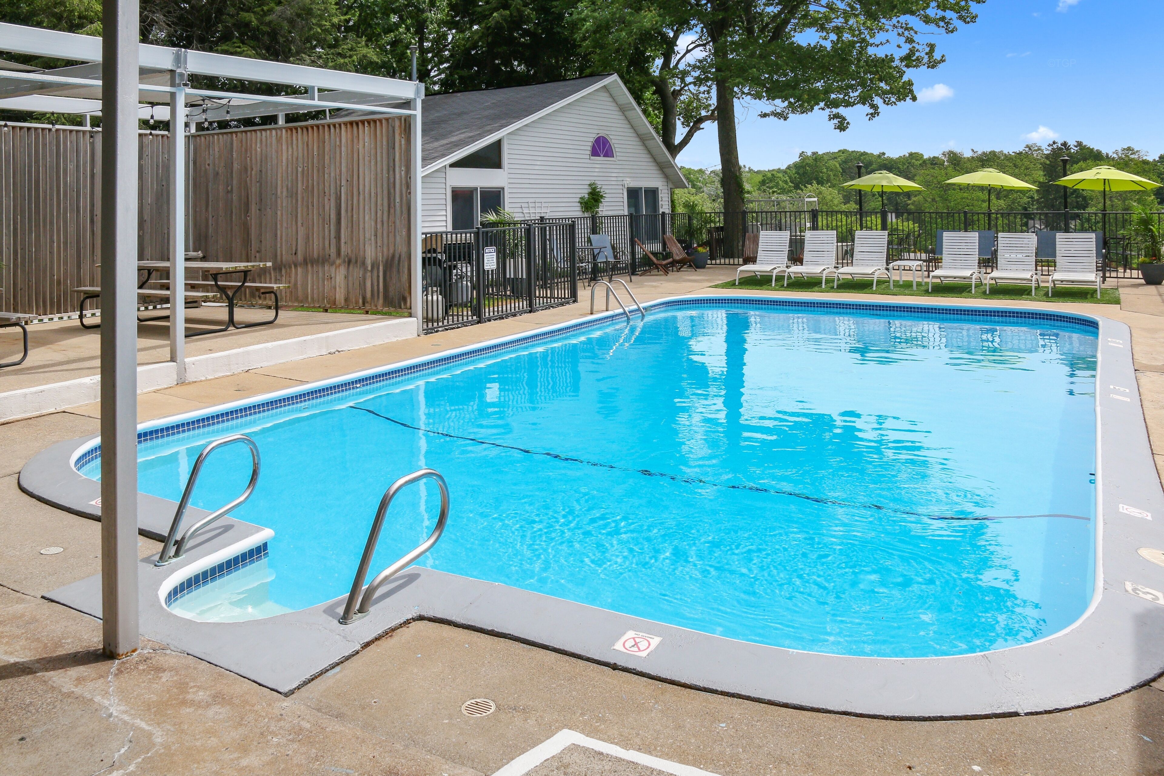 A swimming pool with a wooden fence, lounge chairs, and a pavilion.
