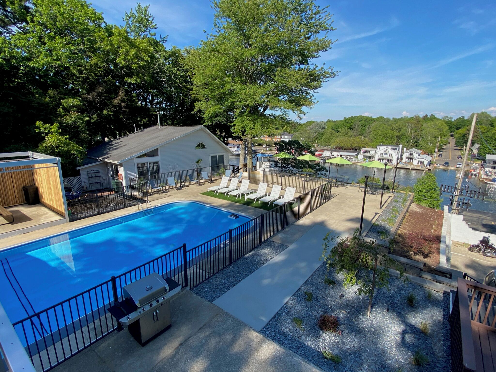 A swimming pool with lounge chairs, a barbecue grill, and a view of a lake and town.