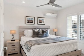 Een slaapkamer met een bed, twee nachtkastjes, een plafondventilator, een airconditioning en twee ingekaderde foto's aan de muur.