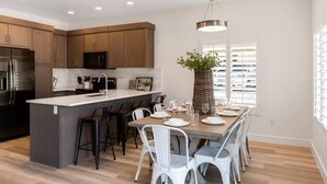 A modern kitchen with wooden cabinets, a stainless steel refrigerator, and a dining area with a large island and white chairs.
