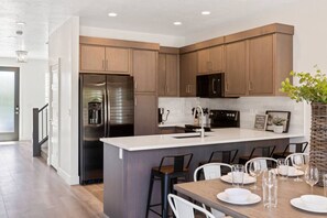 Une cuisine moderne avec des meubles en bois, des appareils en acier inoxydable et un îlot central doté de tabourets de bar.