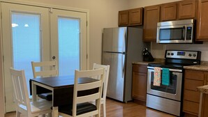 Una cocina con armarios de madera, un refrigerador de acero inoxidable, un microondas, un horno y una mesa de comedor con sillas.