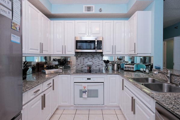 A modern kitchen with white cabinets, a built-in microwave, a dishwasher, and a granite countertop.