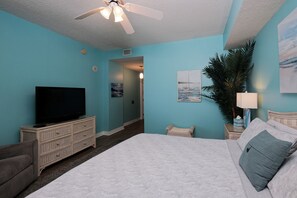 A bedroom with a bed, a television, a ceiling fan, and a plant.