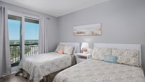A bedroom with two beds, a window with curtains, a nightstand with a lamp, and a framed picture on the wall.