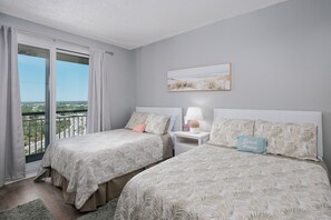 A bedroom with two beds, a window with curtains, a nightstand with a lamp, and a framed picture on the wall.