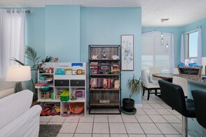 A room with a bookshelf, a desk, a chair, a potted plant, and a window with blinds.