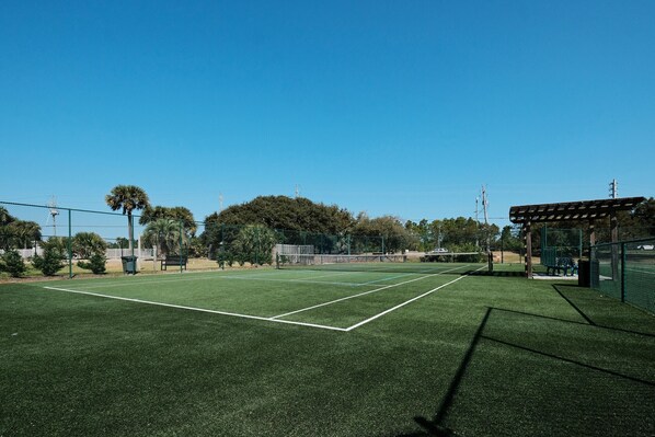 A tennis court with a green surface, surrounded by trees and a fence.